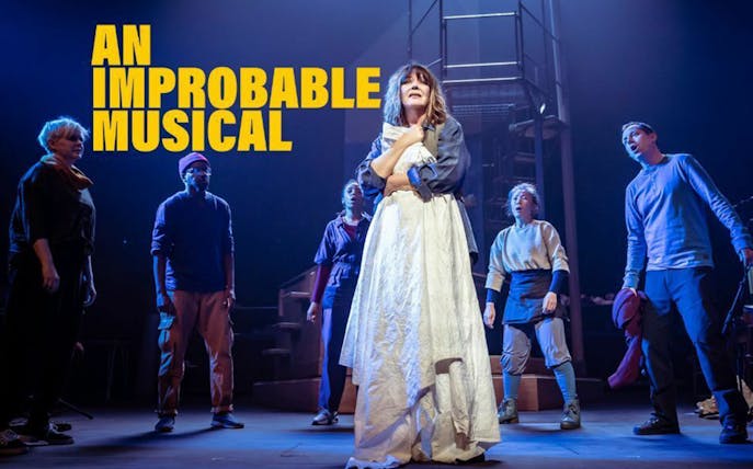 Cast performing on stage in "An Improbable Musical" with dramatic lighting.