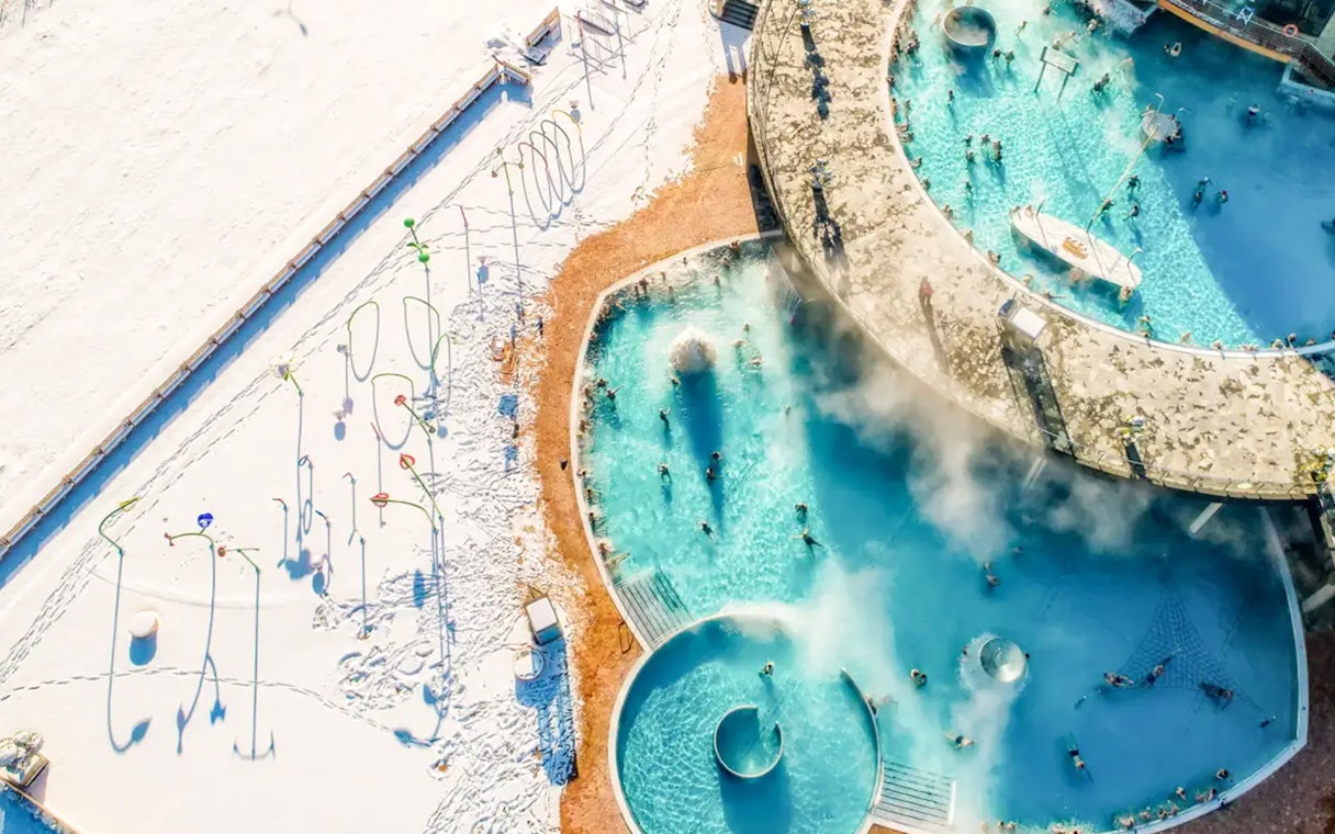 Aerial view of Chocholow Thermal Baths with people enjoying the warm pools surrounded by snow.