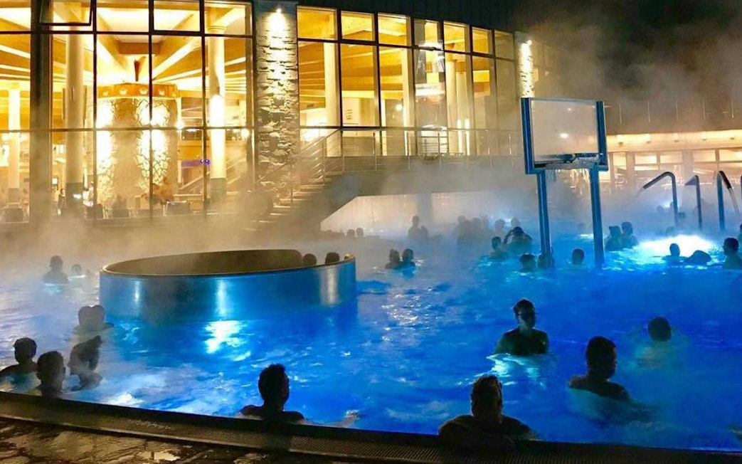 Visitors enjoying the illuminated pools at Chocholow Thermal Baths Saunarium at night.