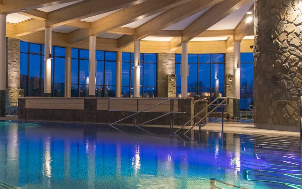 Chocholow Thermal Baths Saunarium pool with stone pillars and large windows at dusk.