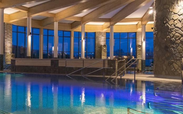 Chocholow Thermal Baths Saunarium pool with stone pillars and large windows at dusk.