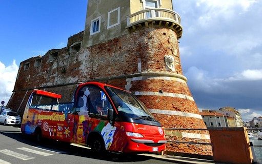Hop-on-hop-off tour bus near historic fortress in Livorno, Italy.