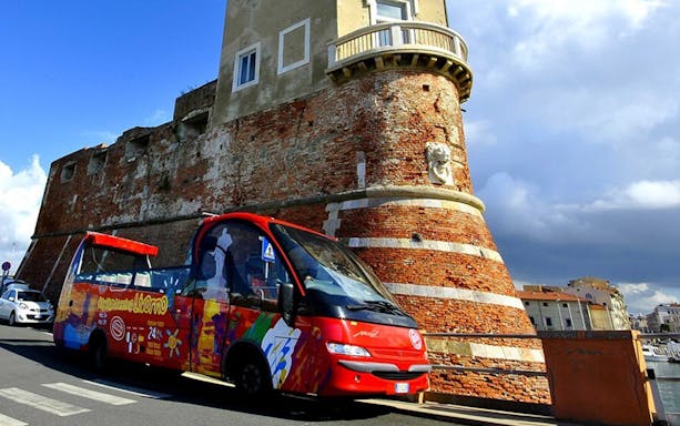 Hop-on-hop-off tour bus near historic fortress in Livorno, Italy.