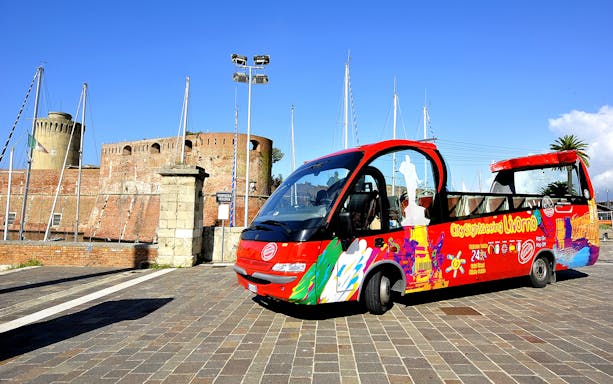 Red sightseeing bus in front of Fortezza Vecchia, Livorno, for 24-hour hop-on-hop-off tour.