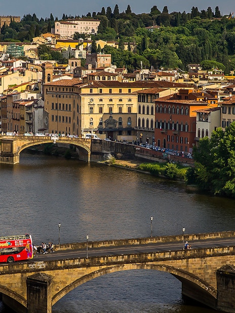 Open-top tour bus crossing a bridge in Florence with cityscape in the background.