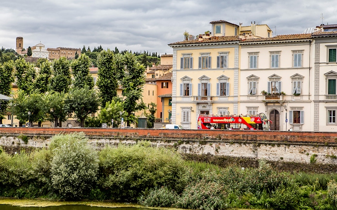 Florence hop-on hop-off bus near historic buildings and lush greenery.
