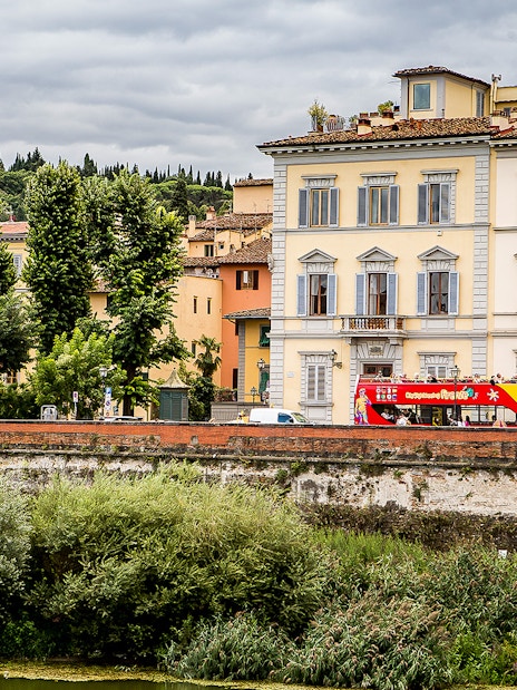 Florence hop-on hop-off bus near historic buildings and lush greenery.