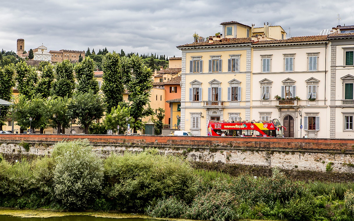 Florence hop-on hop-off bus near historic buildings and lush greenery.
