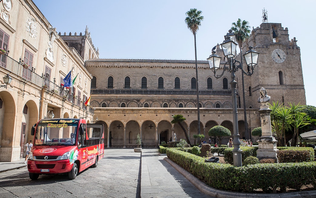 Palermo hop-on hop-off bus in front of historic building with clock tower.
