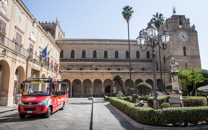 Palermo hop-on hop-off bus in front of historic building with clock tower.