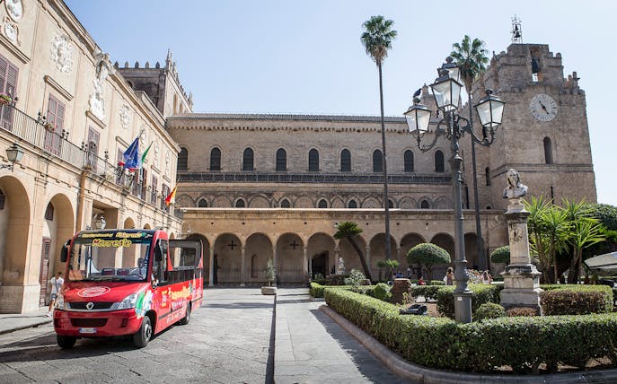 Palermo hop-on hop-off bus in front of historic building with clock tower.