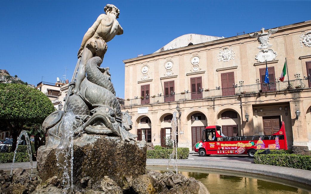 Palermo fountain with City Sightseeing hop-on hop-off bus in front of historic building.