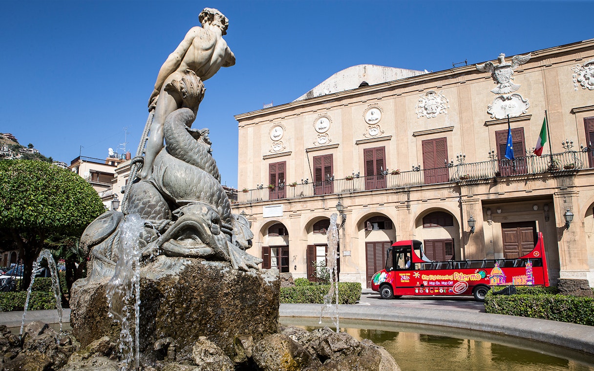 Palermo fountain with City Sightseeing hop-on hop-off bus in front of historic building.