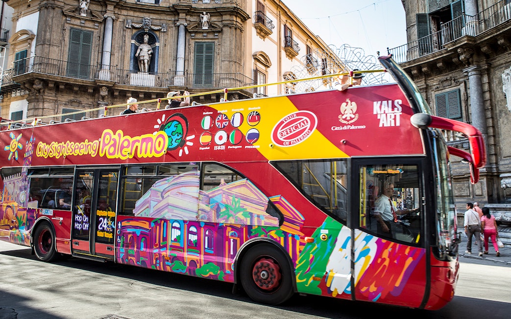Palermo hop-on hop-off bus passing historic building in city center.