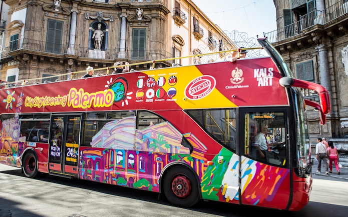 Palermo hop-on hop-off bus passing historic building in city center.