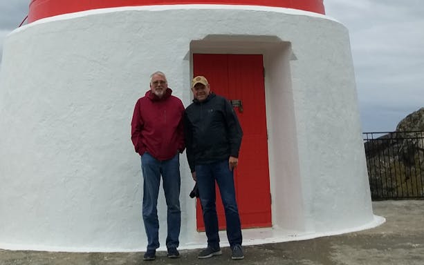 Cape Palliser Lighthouse with two visitors standing in front, Wellington tour.