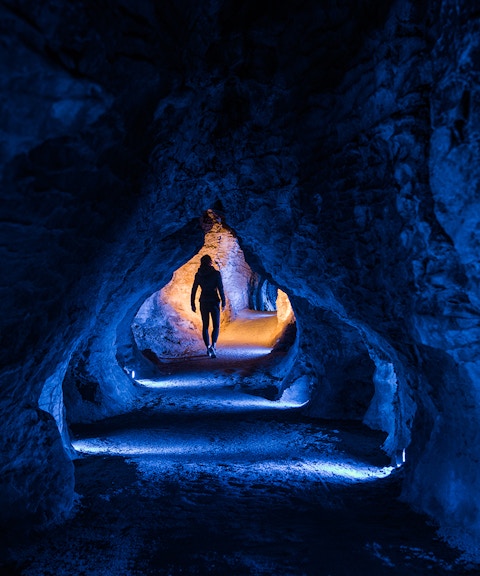 Person walking through illuminated Ruakuri Cave tunnel, New Zealand.