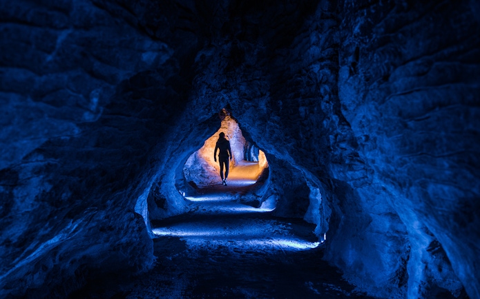 Person walking through illuminated Ruakuri Cave tunnel, New Zealand.