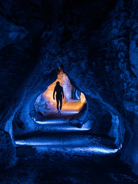 Person walking through illuminated Ruakuri Cave tunnel, New Zealand.