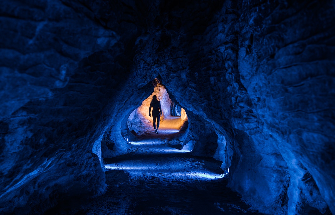 Person walking through illuminated Ruakuri Cave tunnel, New Zealand.