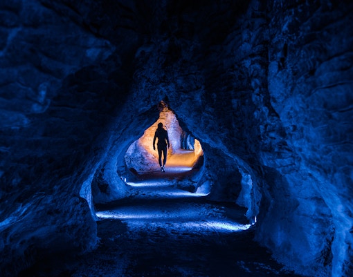 Person walking through illuminated Ruakuri Cave tunnel, New Zealand.