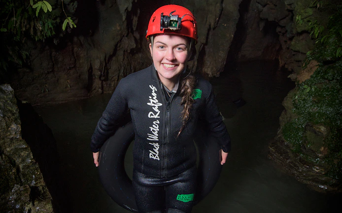 Person in wetsuit and helmet holding an inner tube in Waitomo cave for black water rafting experience.