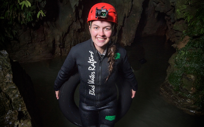 Person in wetsuit and helmet holding an inner tube in Waitomo cave for black water rafting experience.