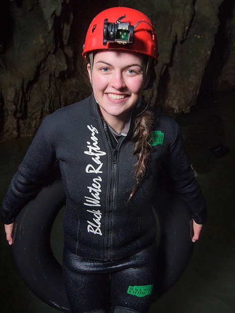 Person in wetsuit and helmet holding an inner tube in Waitomo cave for black water rafting experience.