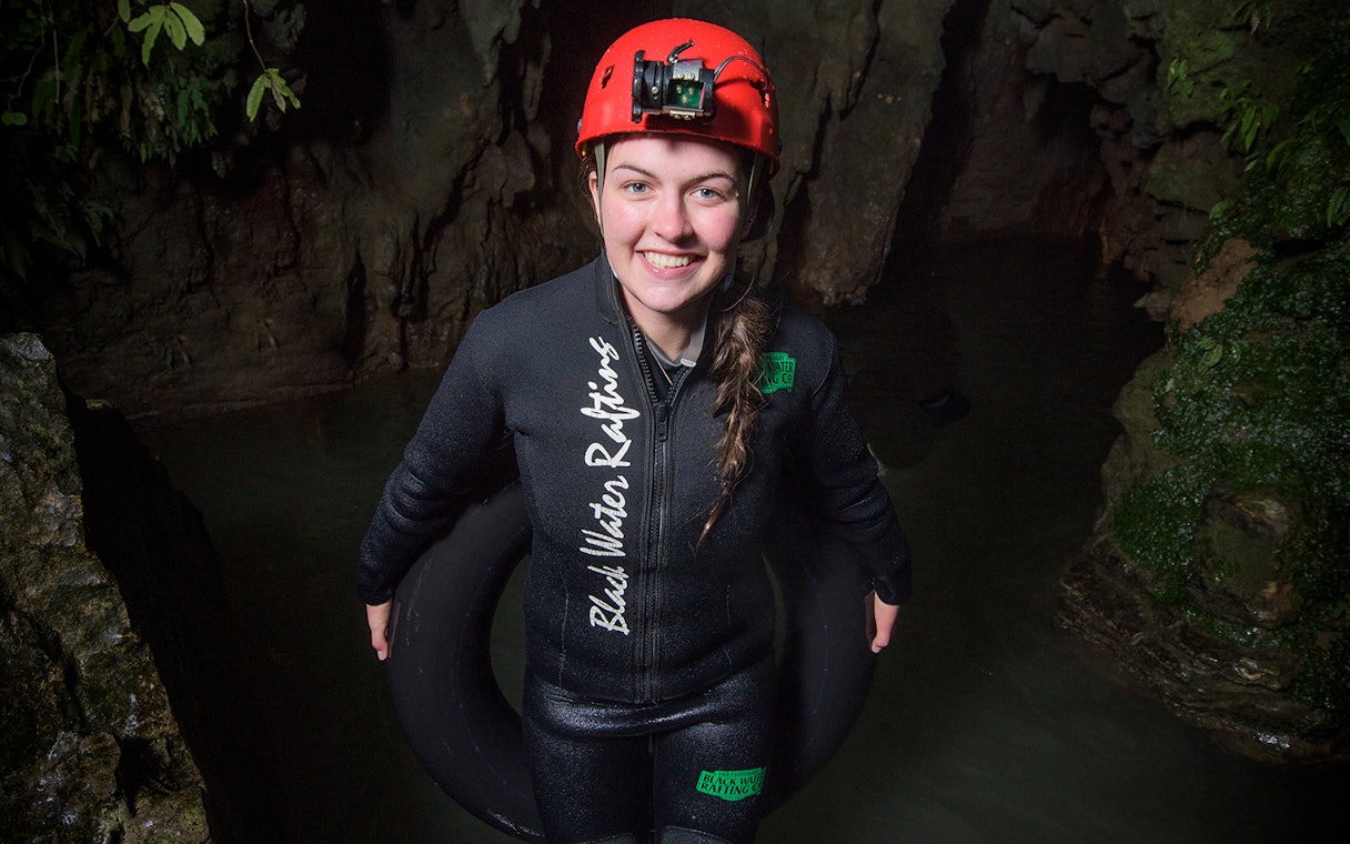 Person in wetsuit and helmet holding an inner tube in Waitomo cave for black water rafting experience.