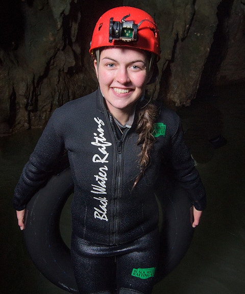 Person in wetsuit and helmet holding an inner tube in Waitomo cave for black water rafting experience.