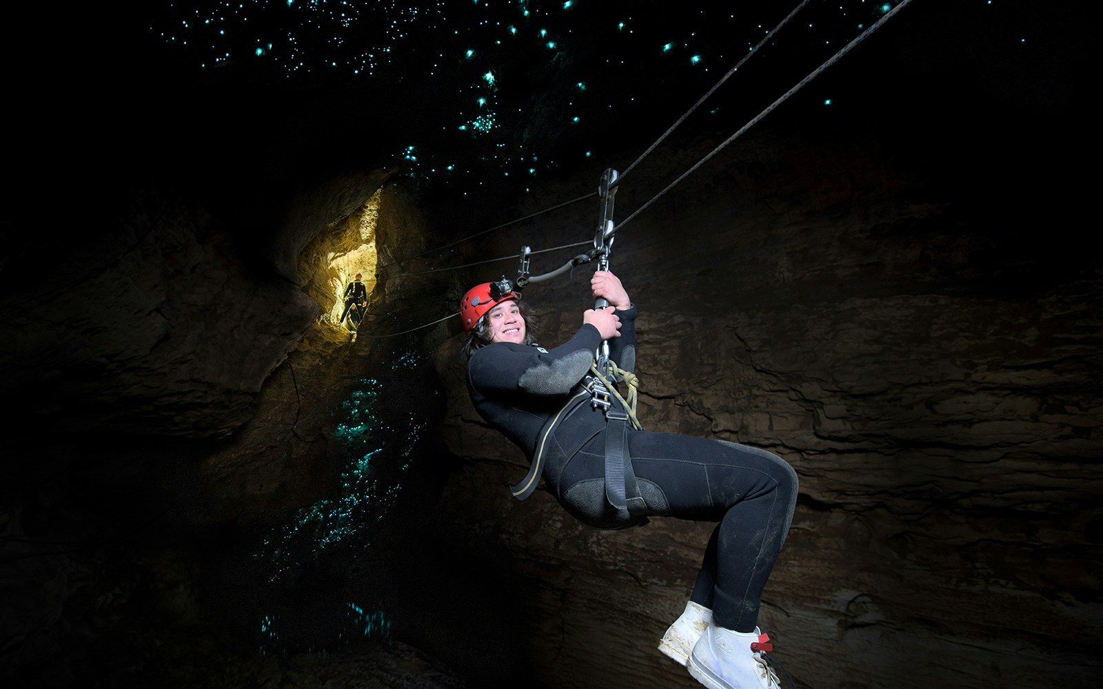 Person ziplining in Waitomo Cave with glowworms illuminating the cave walls.