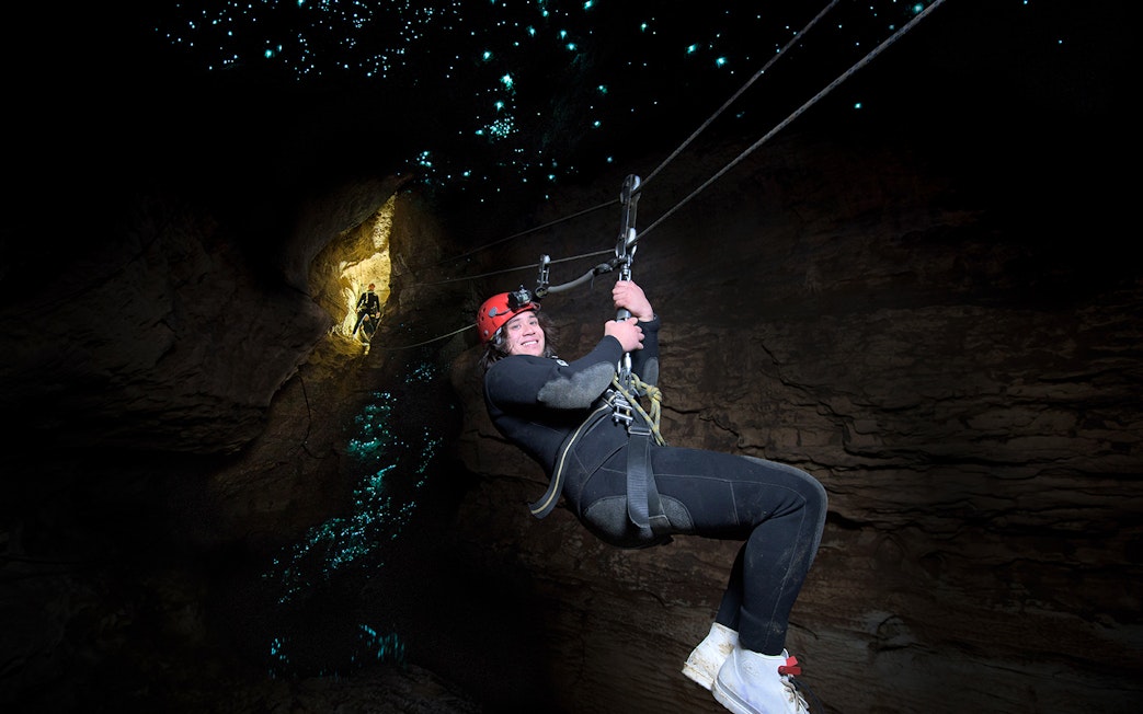 Person ziplining in Waitomo Cave with glowworms illuminating the cave walls.