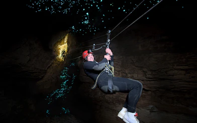 Person ziplining in Waitomo Cave with glowworms illuminating the cave walls.