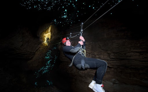 Person ziplining in Waitomo Cave with glowworms illuminating the cave walls.