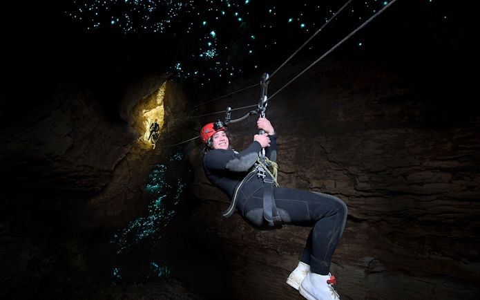 Person ziplining in Waitomo Cave with glowworms illuminating the cave walls.