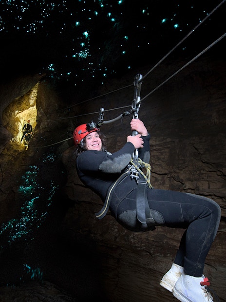 Person ziplining in Waitomo Cave with glowworms illuminating the cave walls.