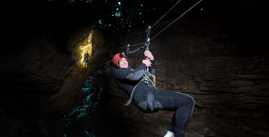 Person ziplining in Waitomo Cave with glowworms illuminating the cave walls.