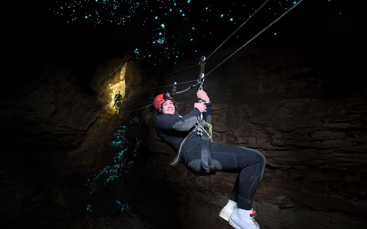 Person ziplining in Waitomo Cave with glowworms illuminating the cave walls.
