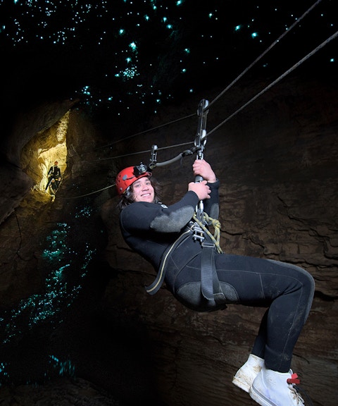 Person ziplining in Waitomo Cave with glowworms illuminating the cave walls.
