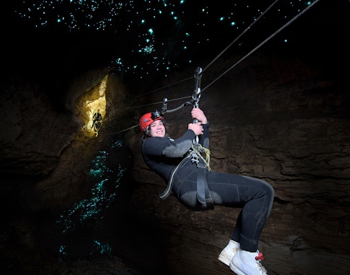 Person ziplining in Waitomo Cave with glowworms illuminating the cave walls.