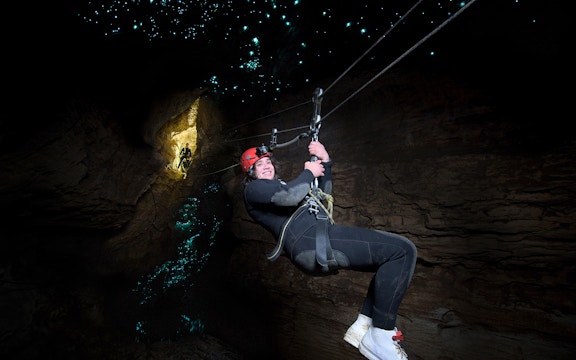 Person ziplining in Waitomo Cave with glowworms illuminating the cave walls.