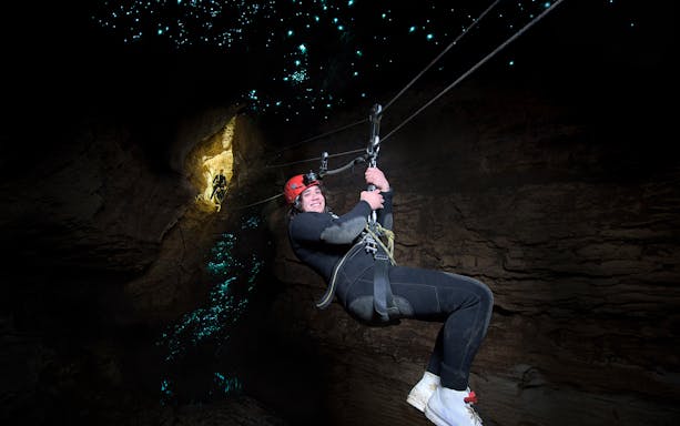 Person ziplining in Waitomo Cave with glowworms illuminating the cave walls.