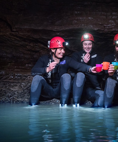 Group enjoying Black Water Rafting in Waitomo cave, wearing helmets and wetsuits.