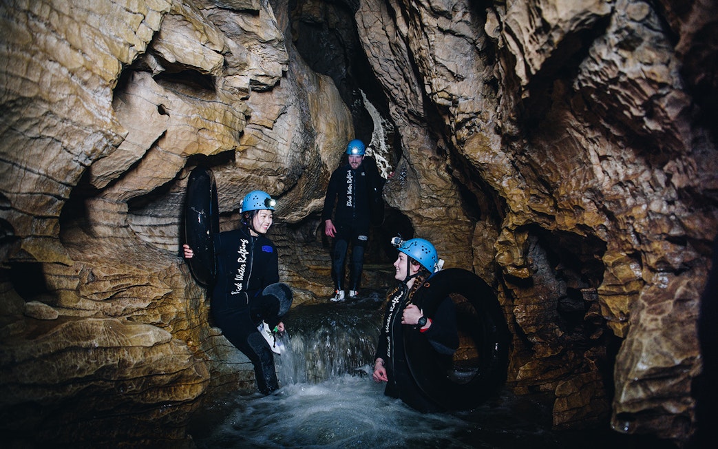Adventurers in wetsuits and helmets explore a cave during a black water rafting tour in Waitomo.