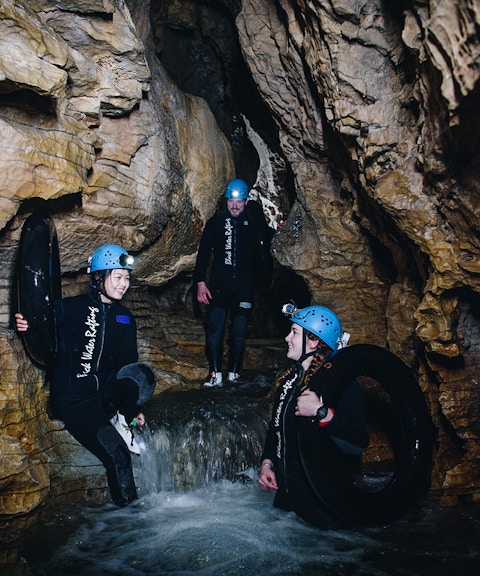 Adventurers in wetsuits and helmets explore a cave during a black water rafting tour in Waitomo.