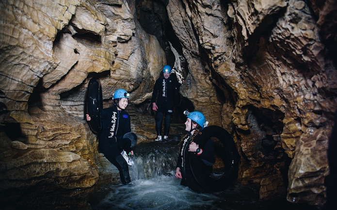 Adventurers in wetsuits and helmets explore a cave during a black water rafting tour in Waitomo.