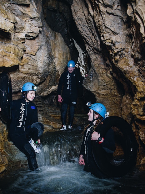 Adventurers in wetsuits and helmets explore a cave during a black water rafting tour in Waitomo.