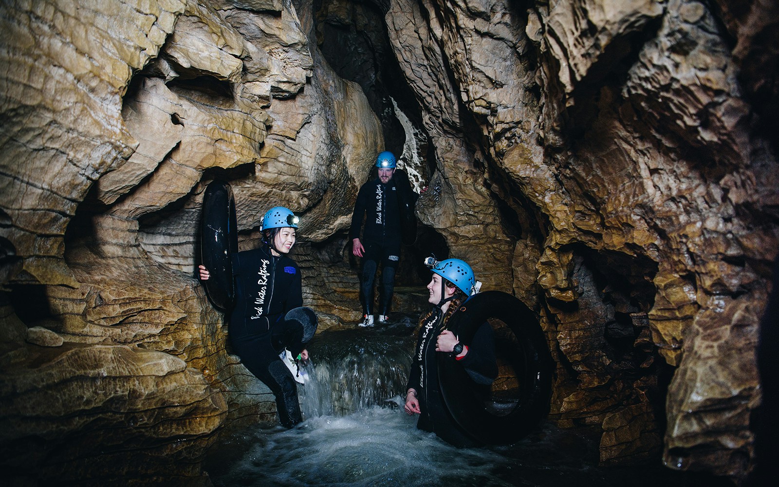 Adventurers in wetsuits and helmets explore a cave during a black water rafting tour in Waitomo.