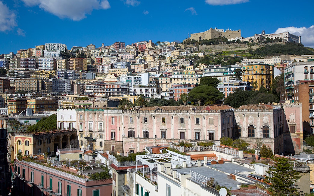 View of Castel Sant'Elmo atop a hill in Naples, Italy, with colorful buildings below.