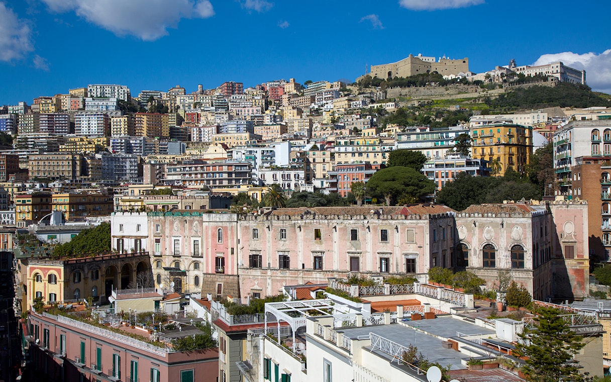 View of Castel Sant'Elmo atop a hill in Naples, Italy, with colorful buildings below.